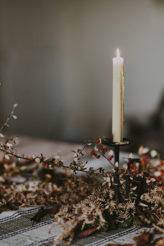 Ett ensamt brinnande stearinljus står i en ljusstake omgiven av torkade blommor.
