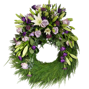En stor blomsterkrans dekorerad med vita liljor, lila rosor och gröna blad på en bas av gröna kvistar.